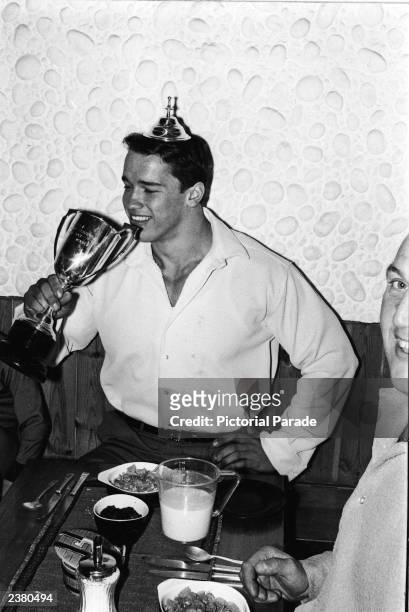 Austrian bodybuilder Arnold Schwarzenegger pretends to drink from his trophy while wearing its lid as a crown after winning the Mr. Universe contest,...