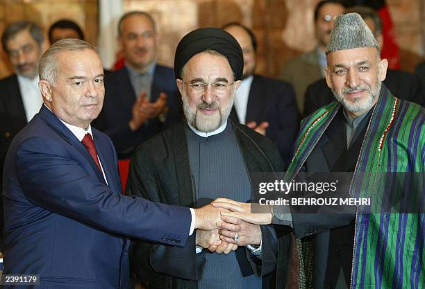 Uzbek President Islam Karimov, Iranian President Mohammad Khatami and their Afghan counterpart Hamid Karzai put their hands together after signing an...