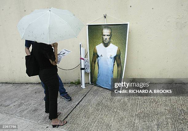 Woman looks at a poster of Spanish club Real Madrid player David Beckham of England on display outside Hong Kong Stadium, 08 August 2003, ahead of...