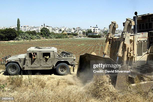 Israeli soldiers watch from their Humvee as an army bulldozer clears the patrol road which runs inside of Israel's security wall August 17, 2003 in...