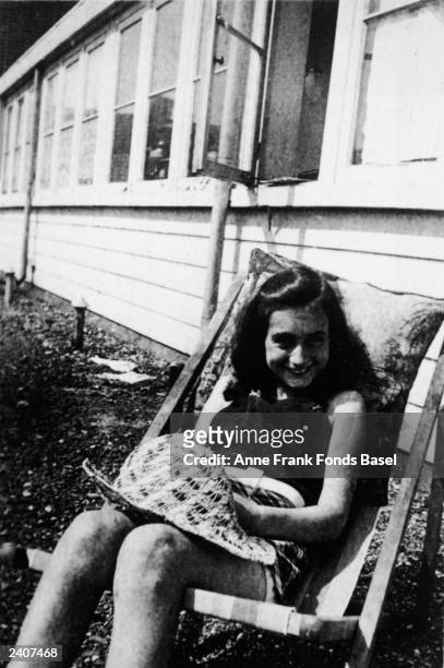 German diarist and Holocaust victim Anne Frank smiles while sitting outdoors in a wooden lawn chair, circa 1939.