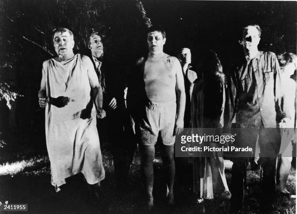 Line of undead 'zombies' walk through a field in the night in a still from the film, 'Night Of The Living Dead,' directed by George Romero, 1968.