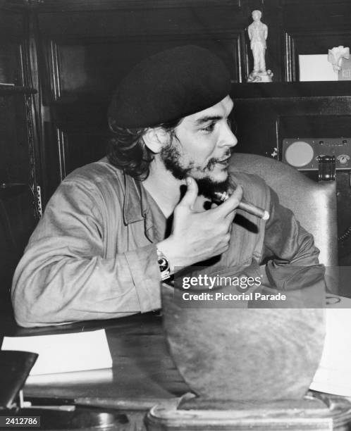 Cuban guerrilla revoutionary leader Ernesto 'Che' Guevara sits at a desk, holding a cigar, late 1950s.