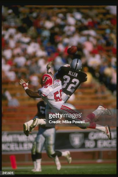 Running back Marcus Allen of the Los Angeles Raiders and linebacker Jesse Tuggle of the Atlanta Falcons jump for the ball during a game at the Los...