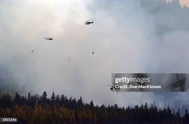 Helicopters battle a wildfire burning in the Okanagan Mountain Park August 26, 2003 near Kelowna, British Columbia, Canada. The fire tore through the...