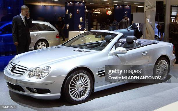 Visitor talks on his mobile as he looks at a Mercedes SL55 AMG car during the first day of the 6th Russian International Motor show "Autosalon 2003"...