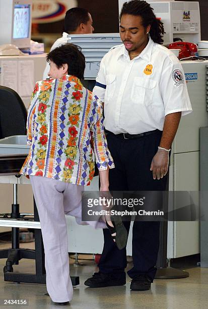 Transportation Safety Administration agent watches as a woman removes her shoes to pass through the metal detector at a security checkpoint at John...