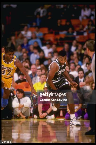 Guard Dennis Scott of the Orlando Magic dribbles the ball down the court as guard Magic Johnson of the Los Angeles Lakers chases after him during a...