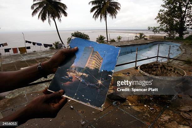 Man juxtaposes a former brochure to the Ducor Palace Hotel with the current view September 2, 2003 in Monrovia, Liberia. The Ducor, which closed when...