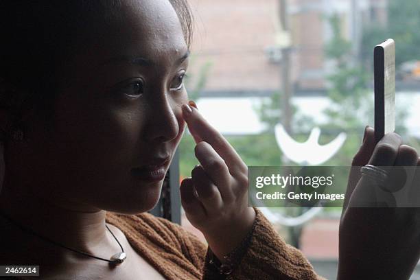 Lucy Hao a jewellery trader, admires her face, which she recently had altered by cosmetic surgery, as she visits a cafe September 4, 2003 in Beijing,...