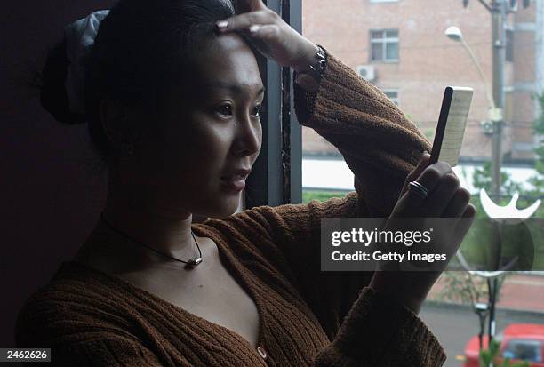 Lucy Hao a jewellery trader, admires her face, which she recently had altered by cosmetic surgery, as she visits a cafe September 4, 2003 in Beijing,...