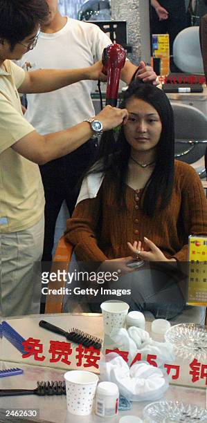 Lucy Hao a jewellery trader, watches herself in a mirror as her stylist blow-dries her hair September 4, 2003 in Beijing, China. Hao is keeping...