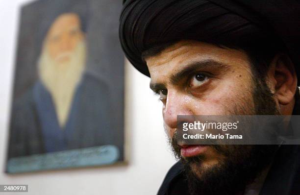 Shiite cleric Sayed Moqtada al-Sadr sits in his offices beneath a portrait of his late father Ayatollah Mohammed Sadeq el-Sadr May 2, 2003 in Najaf,...