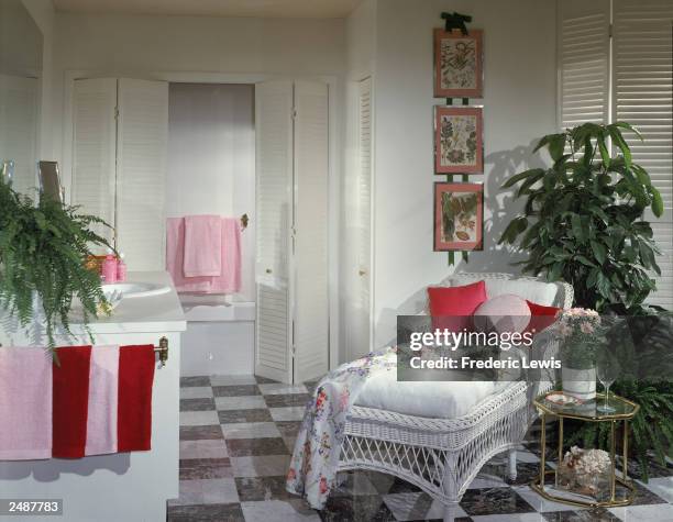 Bathroom interior with an enclosed tub, plants,and a chaise longue with a bathrobe laid out on it, circa 1985.