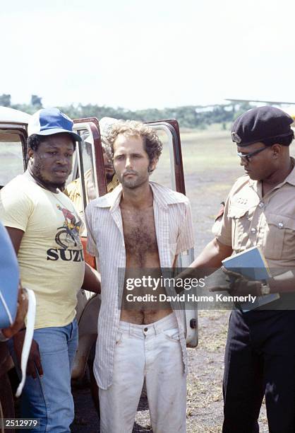 People's Temple follower Larry Layton stands with police following his arrest November 18, 1978 in the shooting of two people on a remote Guyana...