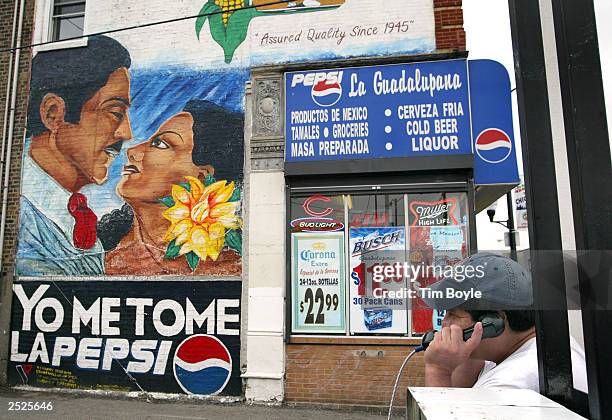 Hispanic man talks on a public phone near a Pepsi wall ad in Spanish September 22, 2003 in Chicago's mainly Hispanic Little Village neighborhood. The...