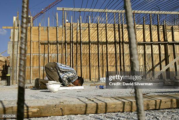 Palestinian laborer bows during his Muslim afternoon prayers at a new housing construction site October 1, 2003 of the West Bank Jewish settlement of...