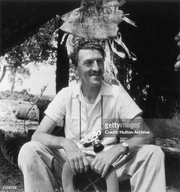 Picture Post Photographer Thurston Hopkins in Tonga, 26th December 1953. Hopkins is sitting under a home-made sign reading 'Picture Post South Seas...