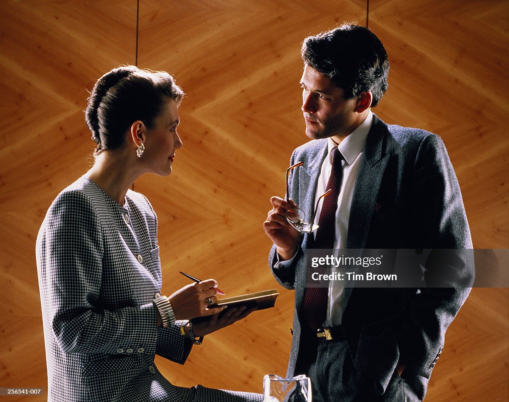 Two executives in discussion,woman sitting on table edge,man standing