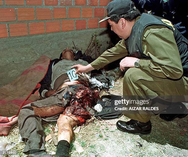 Police officer inspects 09 October 2003 the corpse of miner Luis Atahuchi, hit by the blast of a dinamite stick during clashes between protesters and...