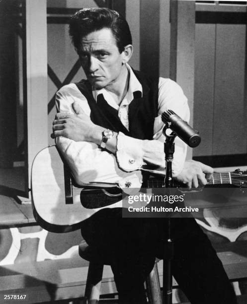 American country singer Johnny Cash sits with an acoustic guitar in a still from the film, 'Road To Nashville,' directed by Will Zenz, 1966.