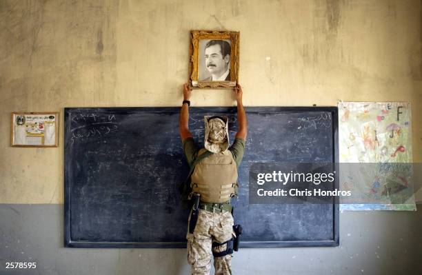 Marine pulls down a picture of Saddam Hussein at a school April 16, 2003 in Al-Kut, Iraq. A combination team of Marines, Army and Special Forces went...