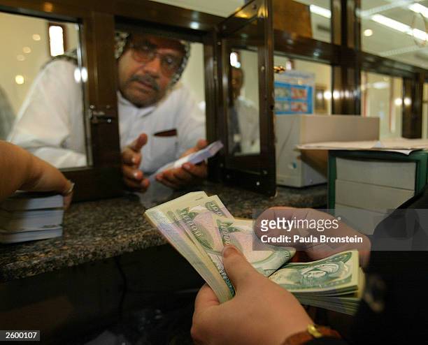 An Iraqi bankteller counts the new Iraqi dinar while dealing with a customer at the Bank of Baghdad October 15,2003 in Baghdad as the currency is...