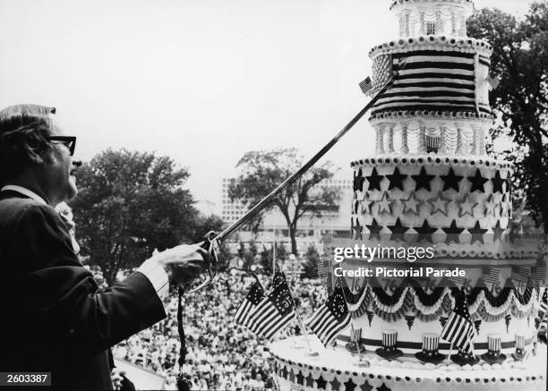 Dr. James B. Rhoads, United States archivist, cuts the giant birthday cake honoring the 200th Anniversary of the signing of the Declaration of...