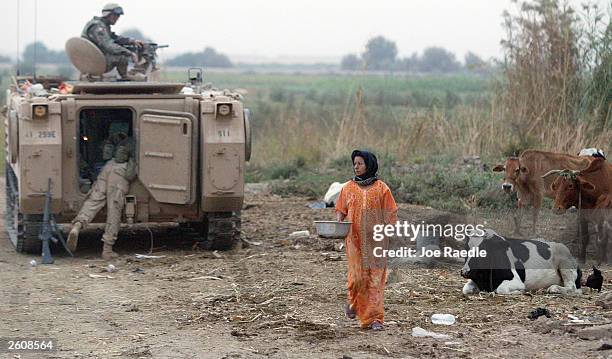 An Iraqi women carries a pail of milk past U.S. Army soldiers from the 299th Engineering Battalion of the Fourth Infantry Division as they carry out...