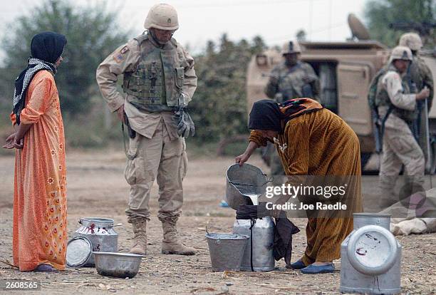 Army Staff Sgt. Neil Schmidt from Houston, Texas of the 299th Engineering Battalion of the Fourth Infantry Division watches Iraqi women as they pour...