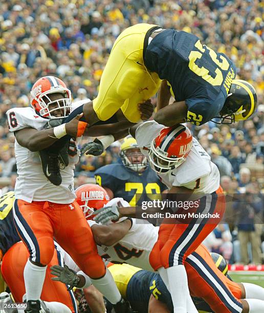 Chris Perry of the Michigan Wolverines jumps over and past Antonio Mason and Marc Jackson of the Illinois Fighting Illini to score his second...