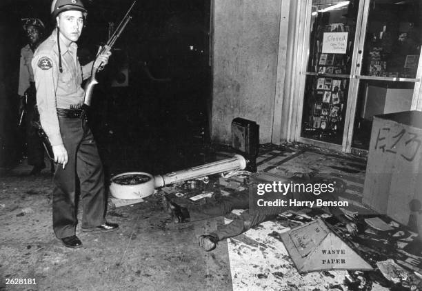 An armed policeman stands beside the body of a Black man during the riots in the Watts district of Los Angeles, 11th-15th August 1965.