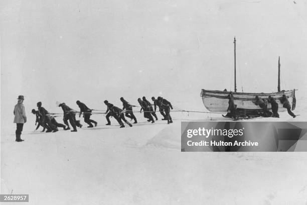 Members of an expedition team led by Irish explorer Sir Ernest Henry Shackleton pull one of their lifeboats across the snow in the Antarctic,...