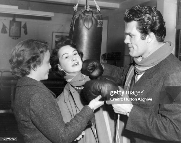 Freddie Mills , ex-world heavyweight boxing champion handing over his gloves to two students of the Queen Mary College. They are securing articles...