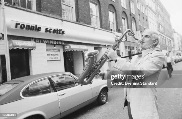 British jazz musician Ronnie Scott playing in the street outside the famous Soho jazz club which he founded, and bears his name. Original...