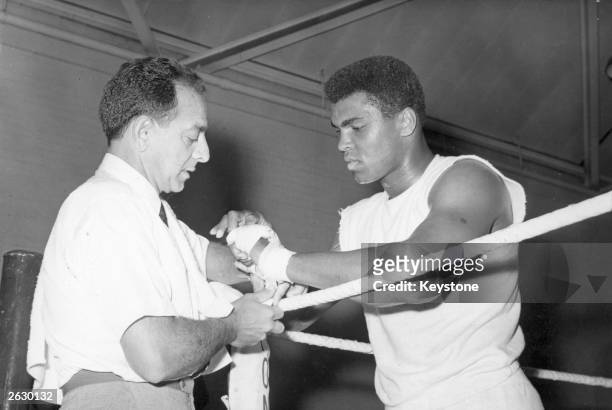 American boxer Muhammad Ali, the world heavyweight champion, has his hands bandaged by his manager Angelo Dundee before the day's training session at...