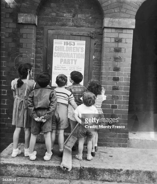Children studying a poster detailing plans for a Coronation party for local blocks of flats in Stepney, east London.