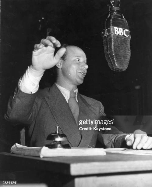 English dramatist, radio producer and presenter Roy Plumley with his hand poised over the finishing bell during the popular BBC Radio programme 'We...