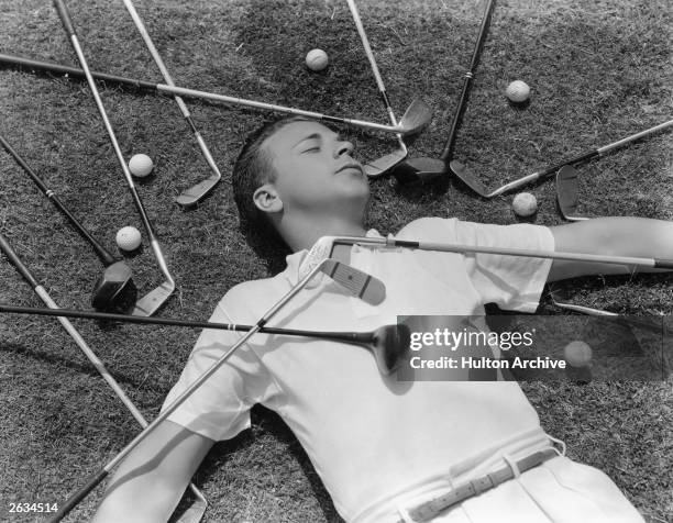 Dick Powell, the American singer, actor and director lying apparently asleep amongst golf equipment. Original Publication: People Disc - HK0437