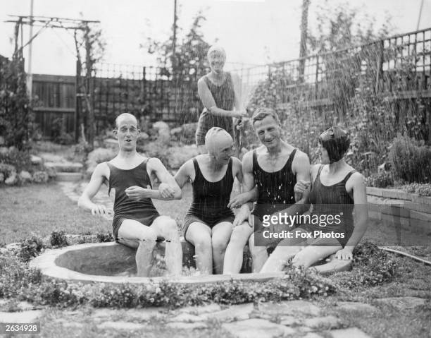 Group of people take refuge from the heatwave with a hose-pipe shower in their garden pond, Streatham, London.