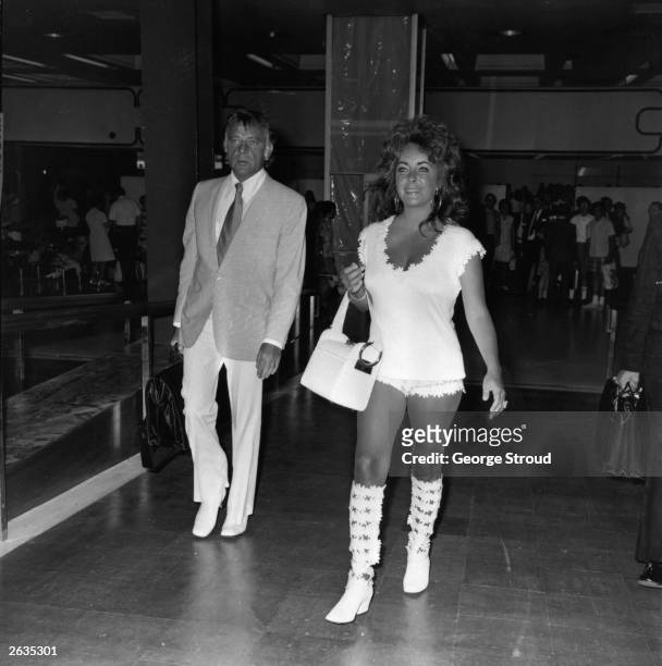 Tanned and smiling, Elizabeth Taylor, the British born American film star walks with Richard Burton the Welsh leading actor through London Airport.