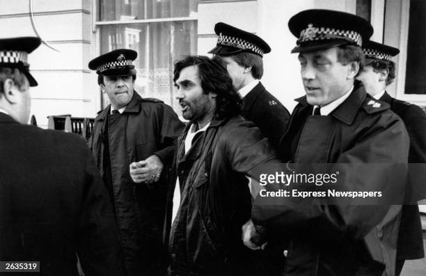 Irish footballer George Best is led away by policemen. He was later accused of drunk driving and assaulting a police officer.