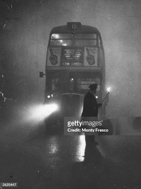 Man guiding a London bus through thick fog with a flaming torch.