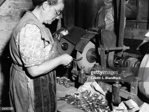 An employee at a factory in Sheffield finishes the prongs of a fork, already roughly cut by machinery, by grinding them on a thin wheel.