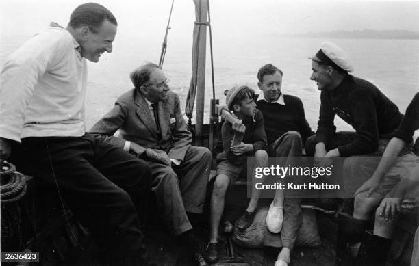 English composer Benjamin Britten , with a boy on his lap, at sea with novelist Edward Morgan Forster , second from left and tenor Sir Peter Pears ,...