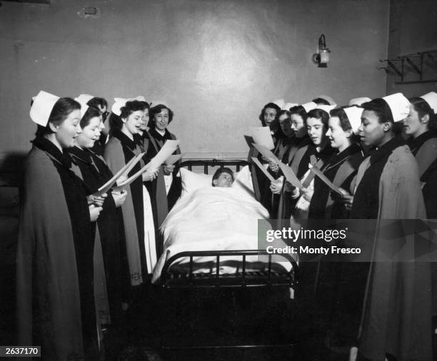 Nurses of Whipps Cross Hospital, in London, singing Christmas carols to one of the patients in bed.