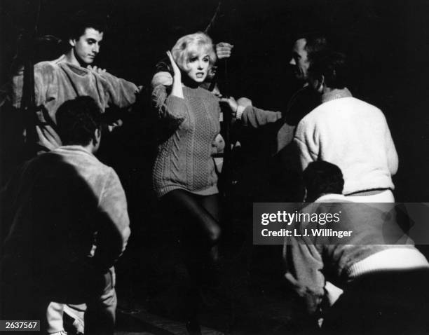 American actress Marilyn Monroe talking to the Jack Cole dancers between takes on the set of the 20th Century Fox film 'Let's Make Love'. The film is...