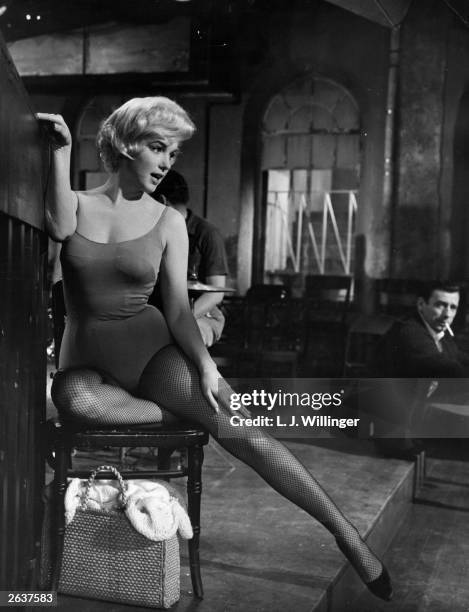 American actress Marilyn Monroe stretches her leg under the watchful eye of Yves Montand on the set of the 20th Century Fox film 'Let's Make Love'....