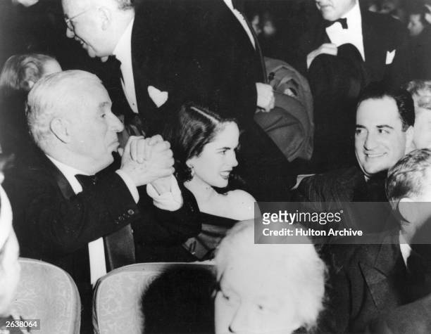 English film actor, screenwriter and director Charlie Chaplin clasping his hands ecstatically whilst attending the premiere of his latest film...