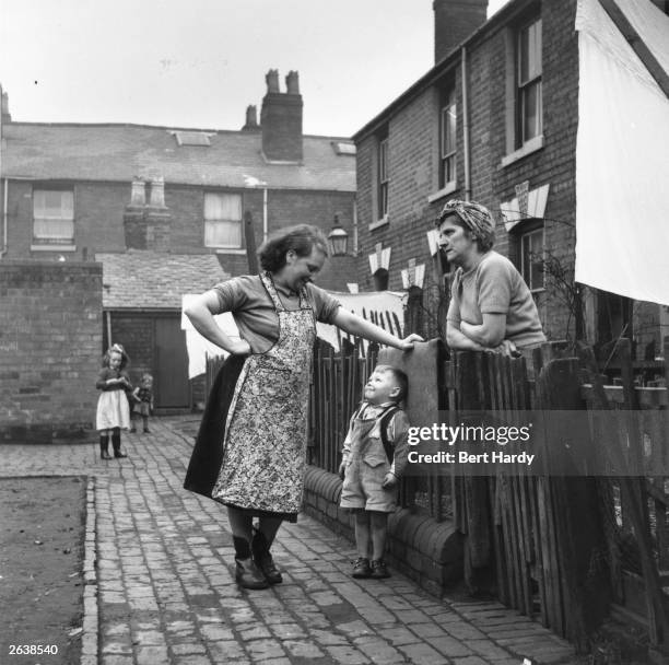 Neighbours chatting at the fence outside their 'back to back' houses in Vaughton Street, Birmingham. Original Publication: Picture Post - 6979 - The...